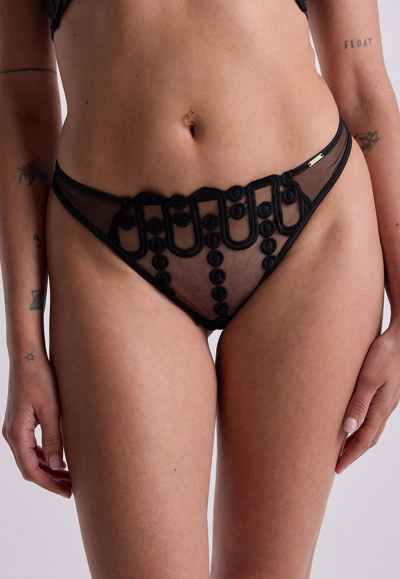 Lingerie noire transparente avec des accents brodés et des boucles complexes, dotée d'une taille basse et d'une texture délicate.