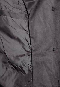 Interno di giacca nera con fodera in raso liscia, tessuto strutturato, quattro bottoni e cuciture pulite; presenta una sottile lucentezza e una vestibilità sartoriale.