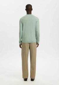 Pull en maille vert menthe à manches longues, col rond et ourlet côtelé, associé à un pantalon beige à jambes larges en tissu lisse.