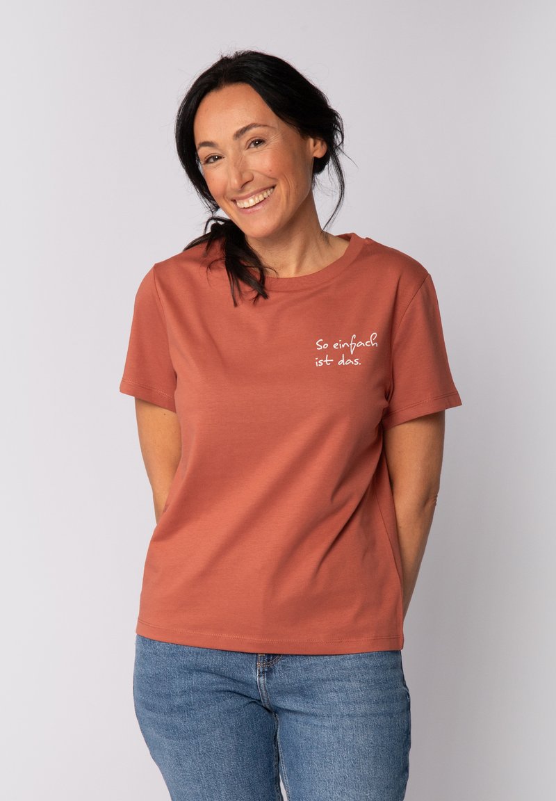 Rostfarbenes T-Shirt mit kurzen Ärmeln, rundem Halsausschnitt und weißem Text "So einfach ist das." Leicht lockere Passform, weiches Baumwollmaterial.