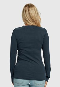 Marineblå ribbestrikket langermet topp med rund hals og tettsittende design, vist fra baksiden med synlige sømmer og en jevn tekstur.