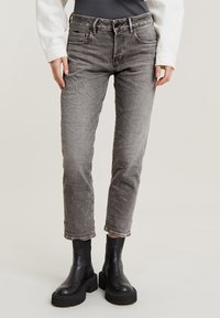 Jean en denim gris à jambe droite, cinq poches, avec un léger effet délavé. Associé à des bottines noires et un haut blanc à manches longues.