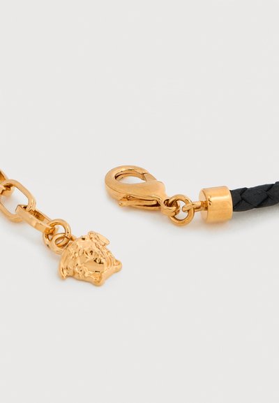 Αλυσίδα χρυσού τόνου με κούμπωμα τύπου αστακού, που έχει μαύρη πλεγμένη δερμάτινη λεπτομέρεια και διακοσμητικό μετάλλιο με λιοντάρι.