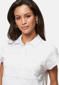 Polo blanc avec un motif rayé texturé, manches courtes et col classique, présentant des accents subtils et une coupe ajustée.