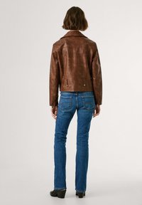 Bruine leren jas met een kraag, getailleerd in de taille, in combinatie met blauwe spijkerbroek. De jas heeft knoopaccenten en heeft een gladde textuur.
