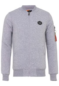 Grijze sweatshirt met een rits aan de voorkant, ribgebreide manchetten en zoom, zijkeuzen en een patchaccent op de linker borst. Heeft een rits op de mouw.