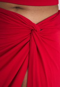 Falda de tejido rojo con un diseño anudado en la cintura, que presenta una textura suave y pliegues drapeados que crean una apariencia en capas.
