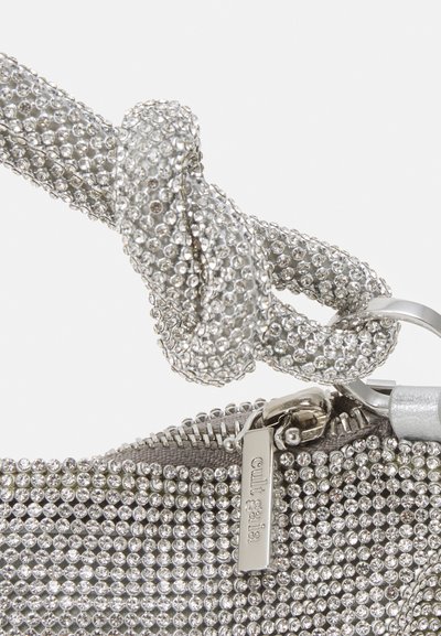 Silverfärgad handväska med en rhinestone-täckt rem, som har en knuten design, dragkedjestängning och en metalletikett med varumärkesnamnet.