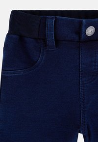 Pantalons en denim bleu foncé avec une ceinture noire côtelée et une fermeture à bouton. Comprend des poches avant et des coutures soignées. Texturé lisse, design décontracté.