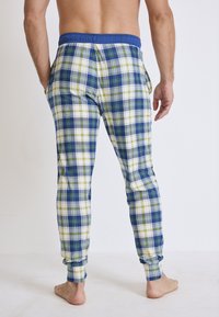 Herrernas rutiga loungebyxor i vitt, blått och grönt. Har elastisk midja och sidofickor. Mjuk tyg med ett rutmönster.