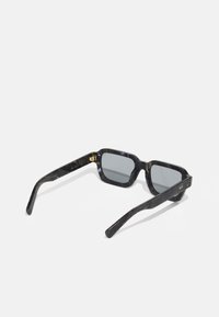 Schwarze Schildkrötenmotiv-Sonnenbrille mit quadratischem Rahmen, grauen Gläsern und goldenen Hardware-Akzenten an den Bügeln. Glatte Textur im gesamten Design.