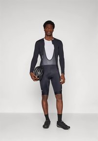 Equipamento de ciclismo composto por uma camisola preta de manga comprida com um painel de rede, calções pretos e um capacete preto, usado com sapatilhas de ciclismo pretas.