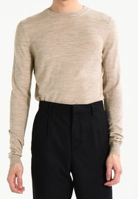 Beiger Strickpullover mit langen Ärmeln und rundem Ausschnitt, kombiniert mit hoch taillierten schwarzen Hosen, mit glatter Textur und maßgeschneiderter Passform.