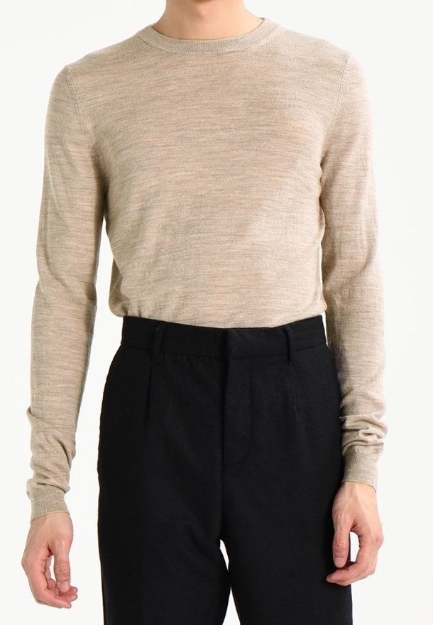 Beiger Strickpullover mit langen Ärmeln und rundem Ausschnitt, kombiniert mit hoch taillierten schwarzen Hosen, mit glatter Textur und maßgeschneiderter Passform.