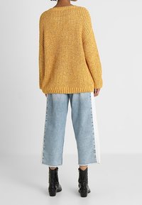 Knitted yellow sweater with a loose fit, featuring a ribbed hem and textured pattern, paired with light blue cropped jeans with white side stripes.