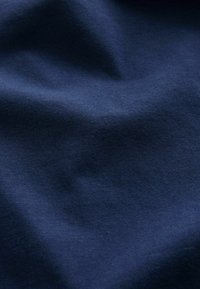 Primer plano de tela suave de color azul oscuro que muestra pliegues sutiles y textura con iluminación uniforme.