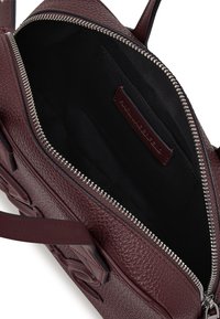 Sac en cuir bordeaux avec un extérieur texturé, fermeture éclair en argent et doublure en tissu noir ; comprend une poche intérieure et une étiquette avec logo.