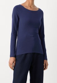 Marinblå långärmad topp med rundad halsringning, slim fit, mjukt tyg och lätt stretch, ihop med texturerade mörka byxor.