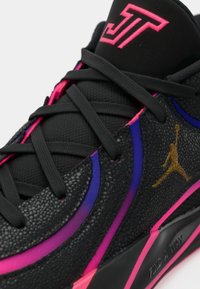 Μαύρο αθλητικό παπούτσι με υφή υλικού, ροζ και μωβ λεπτομέρειες, μαύρα κορδόνια και χρυσό λογότυπο. Διαθέτει σχέδιο με χαμηλό προφίλ.