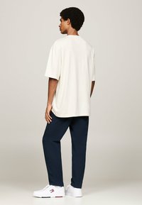 Camiseta beige de gran tamaño con mangas cortas, combinada con pantalones azul marino y zapatillas blancas. Presenta un corte relajado y una textura de tela suave.