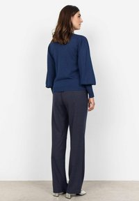 Maglione navy con maniche a palloncino, abbinato a pantaloni scuri con righe sottili. Tessuto liscio e silhouette allungata. Tacchi lucidi completano il look.