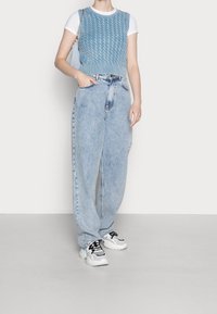 Pull en laine bleu clair à cropped avec une texture côtelée, associé à un jean baggy bleu clair taille haute et des baskets blanches avec des accents noirs.