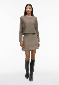 Dvodjelni karirani komplet u smeđoj i crnoj boji koji se sastoji od kratke bluze s dugim rukavima i uske mini suknje, uparen s crnim čizmama do koljena.