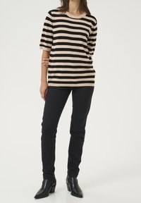 Sort og beige stribet striktop med rund halsudskæring, korte ærmer, parret med sorte tætsiddende bukser og hælede ankelstøvler.