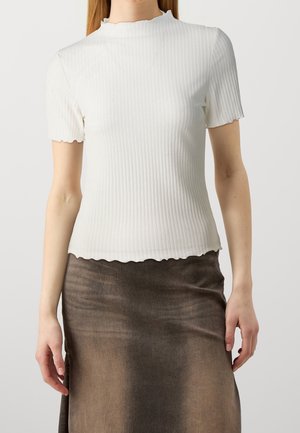Woman wearing a fitted white ribbed short-sleeve top with lettuce-edge hem and a brown gradient skirt against a plain background.