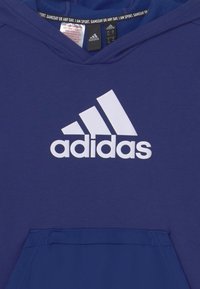 Felpa blu Adidas con logo bianco Adidas sul petto e etichette visibili all'interno del colletto.