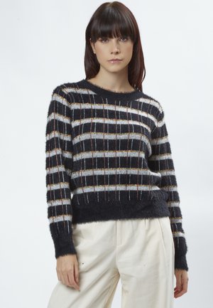 Stribet sweater i sort og hvid med en fuzzy tekstur. Har metalisk guld- og røde accenter i et gittermønster. Rund halsudskæring og afslappet pasform.