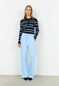 Pruhovaný námornícky modro-biely top s golierom a dlhým rukávom v kombinácii so svetlomodrými širokými nohavicami. Nohavice majú vrecká a detail so zaväzovaním na šnúrku.