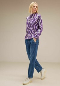 Maglione a motivi viola e grigio con collo alto, abbinato a jeans azzurri chiari e sneakers bianche. Fit casual e rilassato.