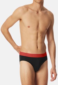 Sorte briefs med en rød elastik, der har brandnavnet. Glat stof med en tætsiddende design og klassisk brief-snit.