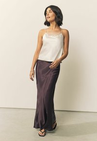 Satin camisole top in cream with lace trim, paired with a flowing dark purple satin skirt. Model wears black flip-flops. Neutral background.