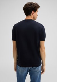 Navyblaues kurzärmliges Strickoberteil mit Rundhalsausschnitt, das eine glatte Textur und eine lockere Passform aufweist, kombiniert mit hellblauen Jeans.