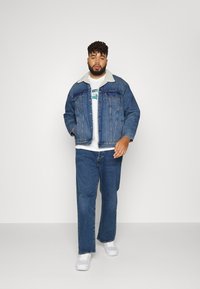 Džinsinis švarkas su šerpa apykakle, mėlynos džinsinės kelnės ir balta marškinėlius su žaliu logotipu. Baltos sportbačiai užbaikite kasdienišką aprangą.