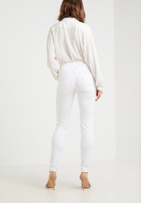 Vita smala jeans med hög midja, med en mjuk, stretchig denimtextur och två bakfickor. Bärs med en lös vit blus.