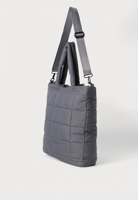 Borsa tote grigia trapuntata con manici imbottiti e tracolla regolabile su sfondo bianco.