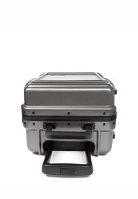 Grey hard-shell suitcase with a textured finish, featuring a retractable handle, multiple reinforced corners, and durable black hardware.