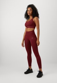 Burgunder sports-bh og høye leggings, ribbet tekstur, tettsittende design. Svarte joggesko med snøring.