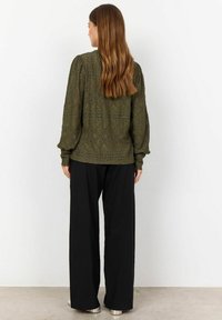 Blusa verde oliva a maniche lunghe con design ad occhiello e maniche a puffo, abbinata a pantaloni neri a gamba larga e stivaletti argentati.