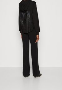 Felpa nera con una schiena scintillante di paillettes, abbinata a pantaloni neri larghi. Il tessuto sembra morbido e la silhouette è rilassata e moderna.
