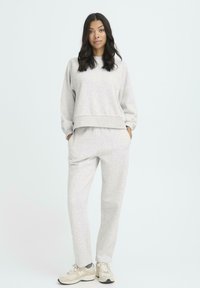 Sudadera gris claro y joggers a juego, fabricados en una tela suave. Presenta un corte relajado, puños anchos y bolsillos laterales. Las zapatillas completan el conjunto.