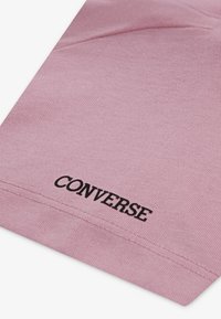 Ροζ βαμβακερό ύφασμα με ριγωτή υφή, με μαύρο λογότυπο "CONVERSE" τυπωμένο κοντά στο τελείωμα. Ο σχεδιασμός είναι απλός και μοντέρνος.