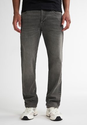 Jeans en denim gris avec une coupe droite, design à cinq poches, décoloration subtile et coutures contrastées, associés à des chaussures de sport blanches.