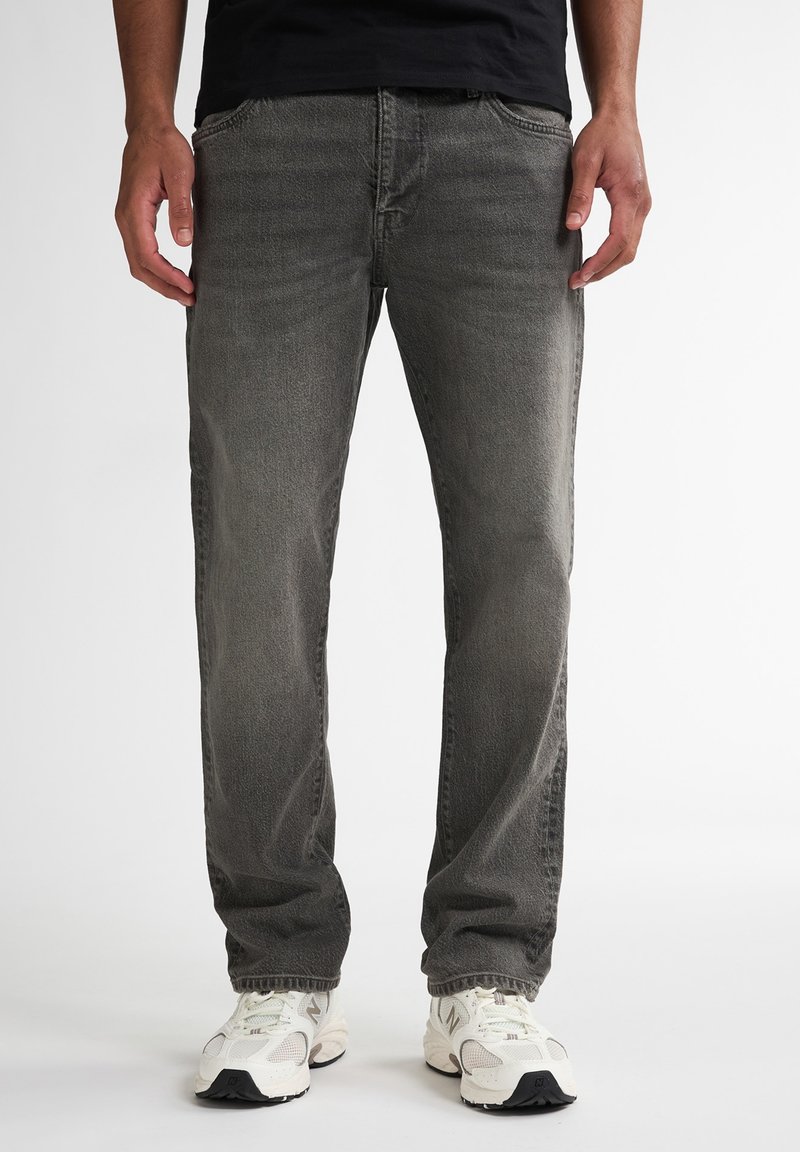 Jeansi din denim gri cu o croială dreaptă, design cu cinci buzunare, estompare subtilă și cusături în contrast, asortați cu adidași albi.