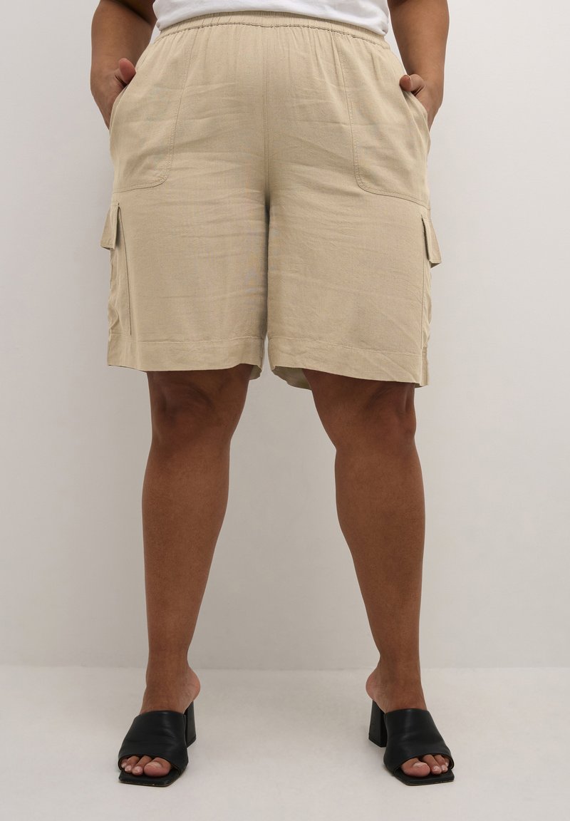 Beige cargo-shortsit, joissa on sivutaskut ja elastinen vyötärö, valmistettu kevyestä kankaasta. Yhdistetty mustiin avokärkisiin korkokenkiin.