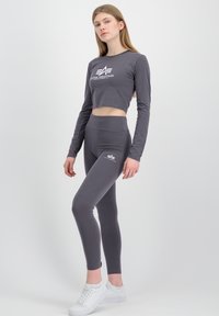 Grå, avkortet langermet topp og matchende høyt liv leggings med hvit logo detalj, paret med hvite sneakers. Glatt, elastisk stoff.