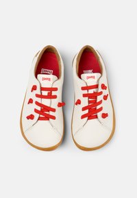 Vita läderskor med röda snören, rund tå och brunt gummisula. Har hjärtformade detaljer nära snören och varumärkesetiketter inuti.